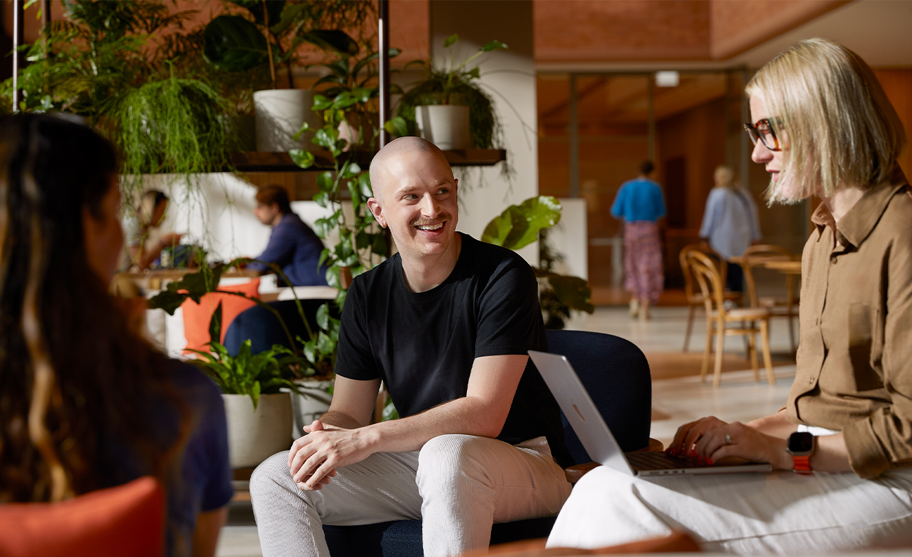 Tre Apple-ansatte, en av dem med en MacBook, sitter i hver sin lenestol på en Caffè Macs og snakker sammen.