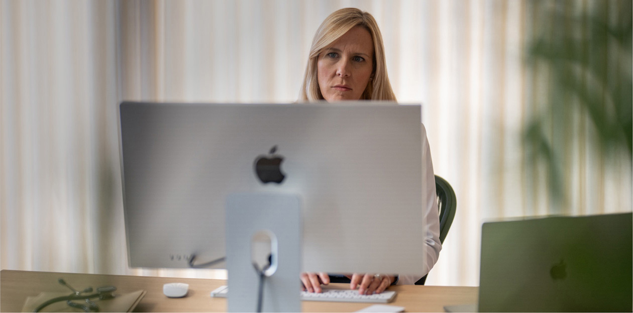 Una dottoressa che guarda lo schermo di un iMac seduta alla sua scrivania.