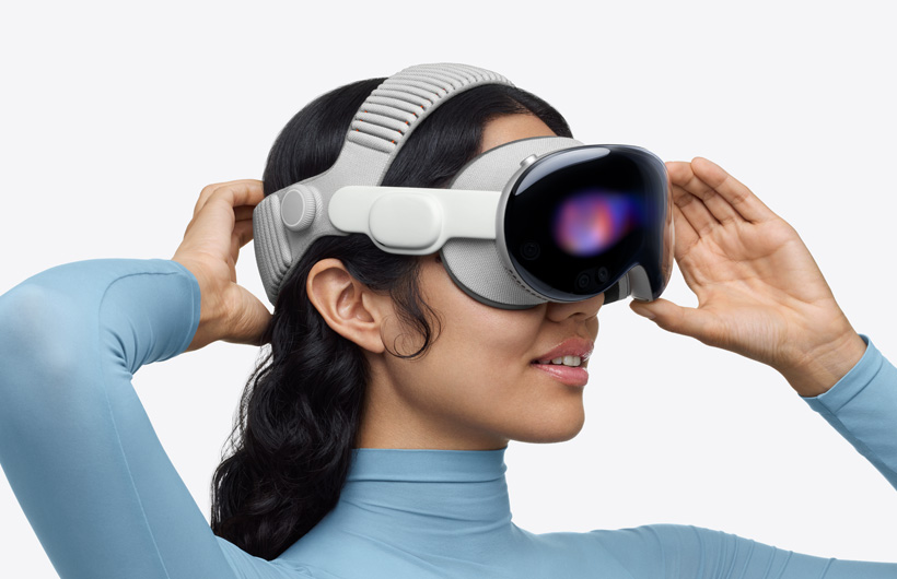 Eine Person trägt die Apple Vision Pro trägt mit dem Dual Band aus Strickgewebe; das obere Band umspannt den Kopf oben, eine Hand der Person befindet sich hinter dem Kopf auf dem unteren Band, die andere Hand auf dem Rahmen aus einer Aluminiumlegierung