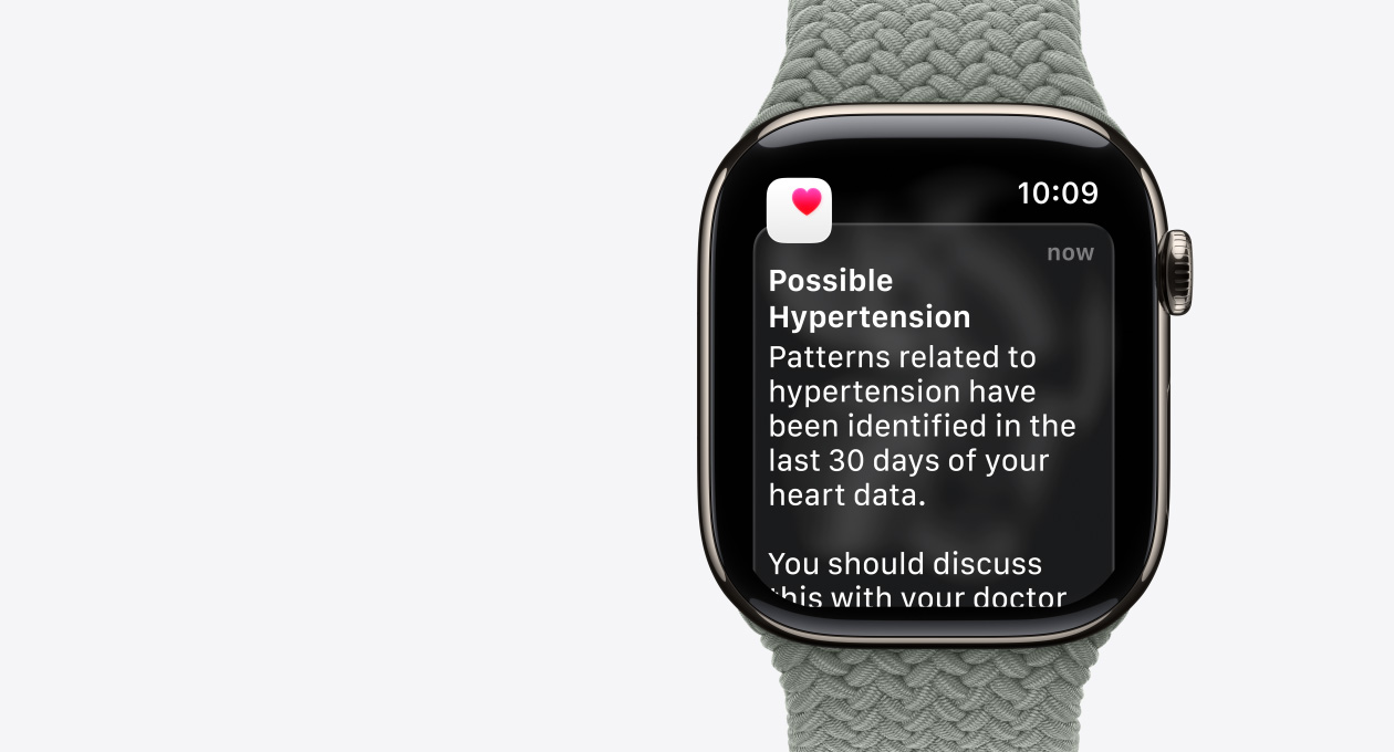 Apple Watch Series 11, prirodna boja, kućište od titanija, obavijest o mogućoj hipertenziji, ružičasto srce u bijelom okviru, vanjska desna strana, Digital Crown, remen, pletena zelenkasto siva narukvica Solo