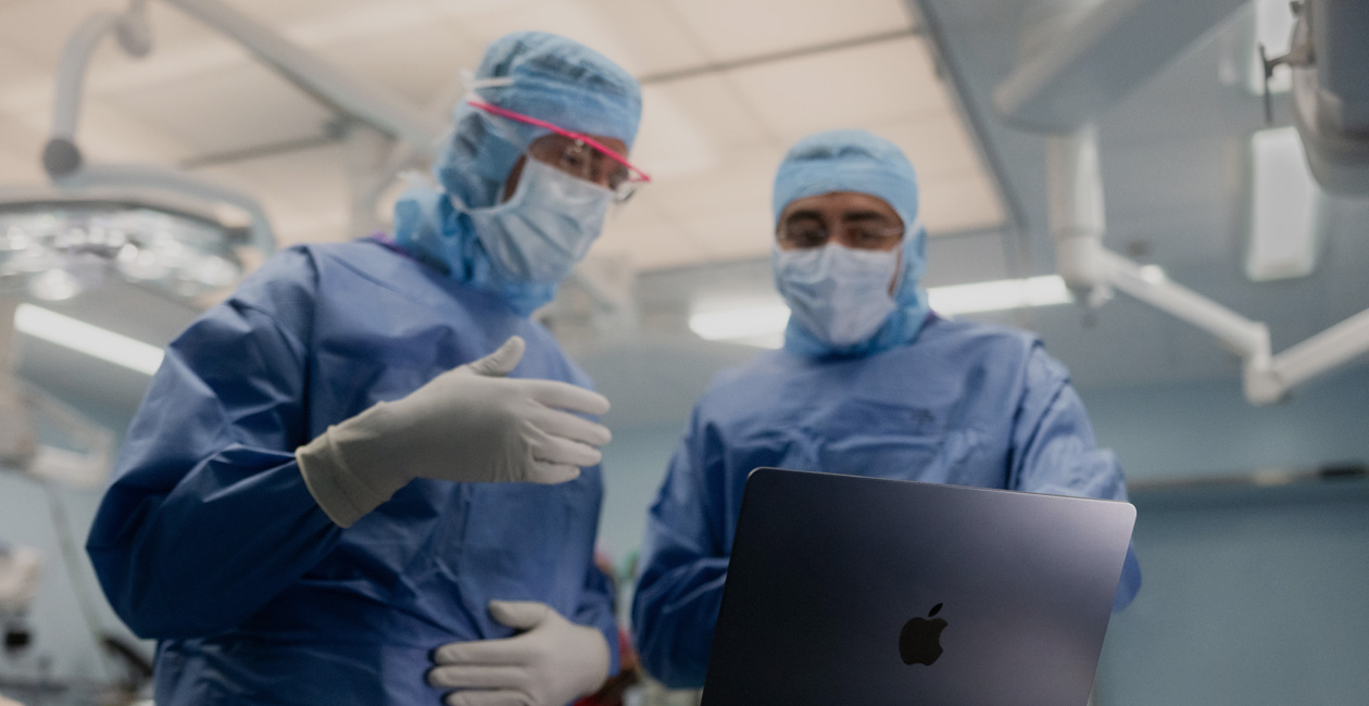 Dos personas en un quirófano comentan lo que aparece en la pantalla de un MacBook Pro.