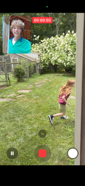 iPhone 17 met op het scherm een Dual Capture-video, opgenomen met zowel de camera aan de achterkant als aan de voorkant, van een jong rennend meisje terwijl een man toekijkt