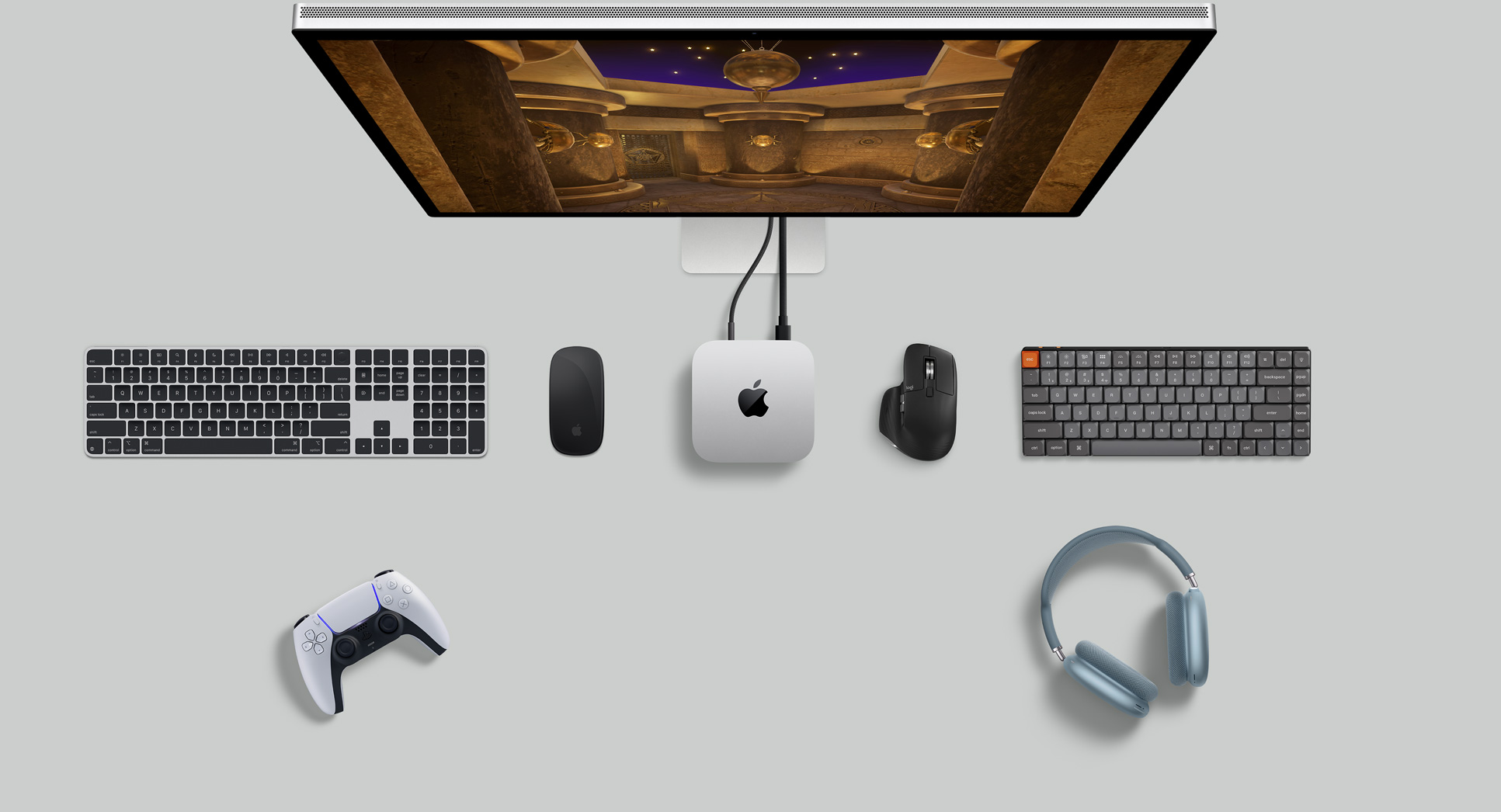 Κάτοψη ασημί Mac mini σε διαμόρφωση γραφείου με οθόνη, ασύρματα πληκτρολόγια, ασύρματα ποντίκια, χειριστήριο παιχνιδιών και AirPods Max