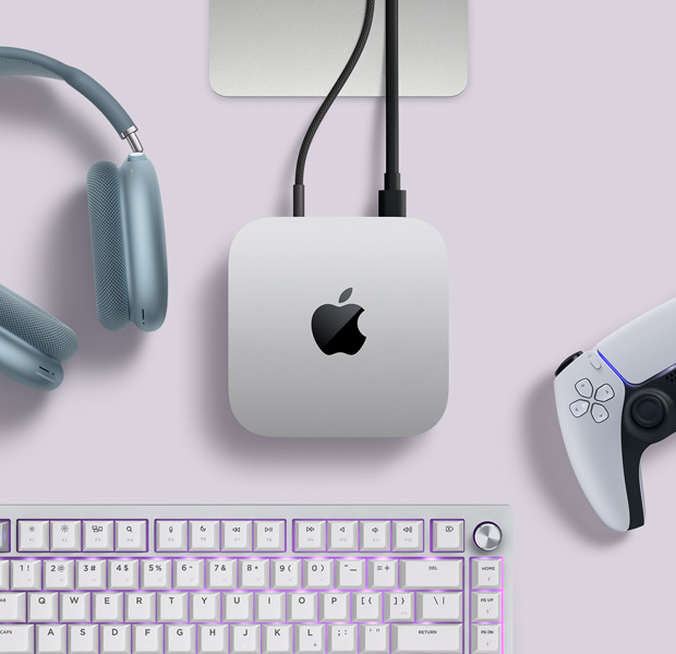 Κάτοψη ασημί Mac mini, με δύο καλώδια συνδεδεμένα στις πίσω θύρες, δίπλα σε μπλε AirPods Max, ασημί Magic Keyboard και ασύρματο χειριστήριο παιχνιδιών