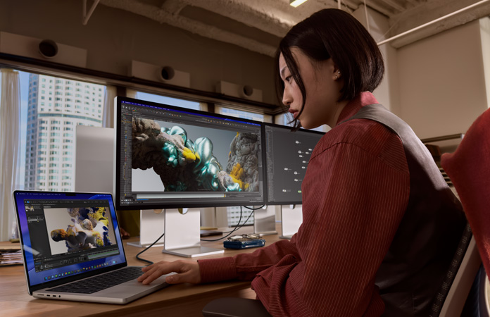 Una persona trabaja en una oficina con una MacBook Pro conectada a un monitor Studio Display XDR